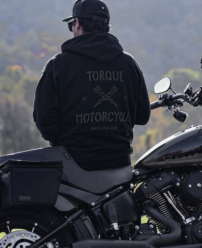 Man sits on his parked motorcycle and is wearing his black Torqued Motorcycle Co Black Hoodie